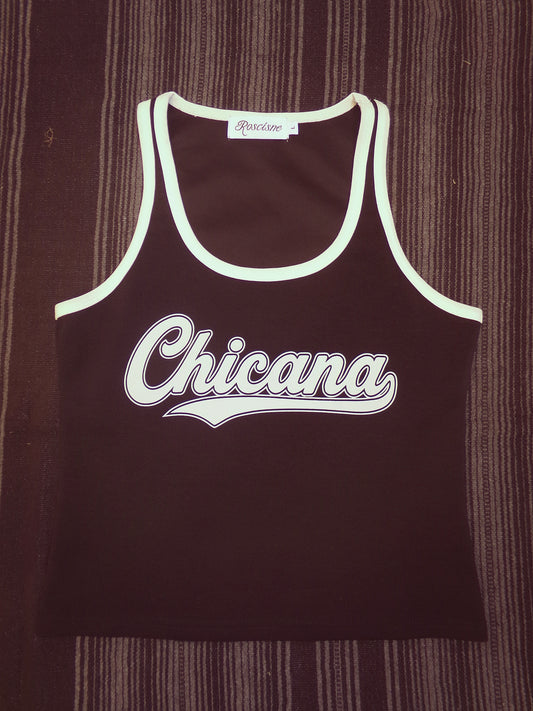 A black 70's style tank top with white trim and the word 'Chicana' printed across the front in white script, laid flat on a serape background.