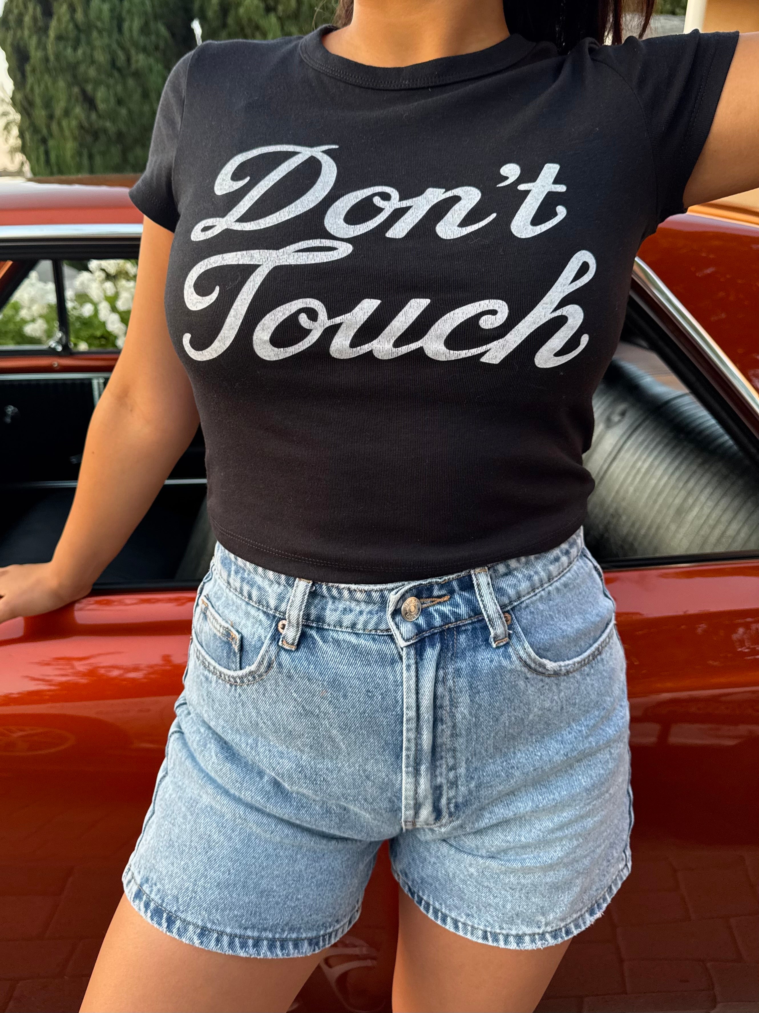 Person wearing a black t-shirt with 'Don't Touch' text in front of an orange lowrider car.