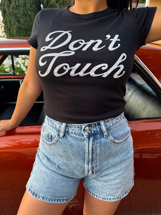 Person wearing a black t-shirt with 'Don't Touch' text in front of an orange lowrider car.
